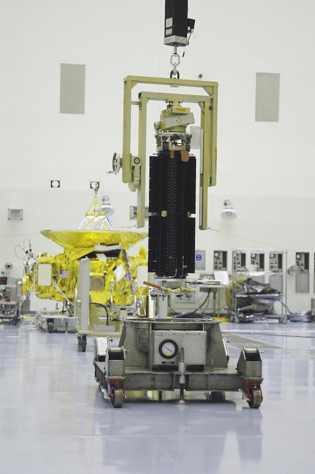 V Kennedyho kosmickém středisku NASA jeřáb zvedá radioizotopový termoelektrický generátor (RTG), který bude instalován v kosmická sondě New Horizons v pozadí. Zdroj: NASA