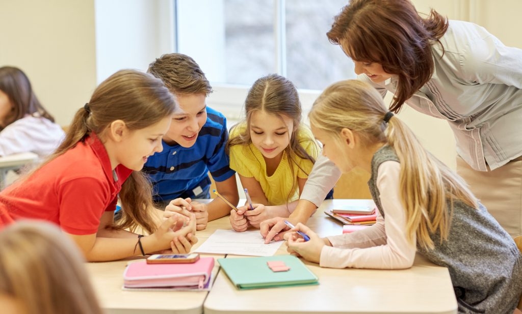 education, elementary school, learning and people concept - teacher helping school kids writing test in classroom