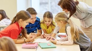 education, elementary school, learning and people concept - teacher helping school kids writing test in classroom