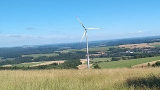 Decentralizované větrné turbíny a farmy by i u nás mohly přispět k přechodu k nízkoemisní elektroenergetice. V popředí osamělá turbína v Jizerských horách, v pozadí nalevo od ní pak skupina turbín v Polsku. (Foto Vladimír Wagner).